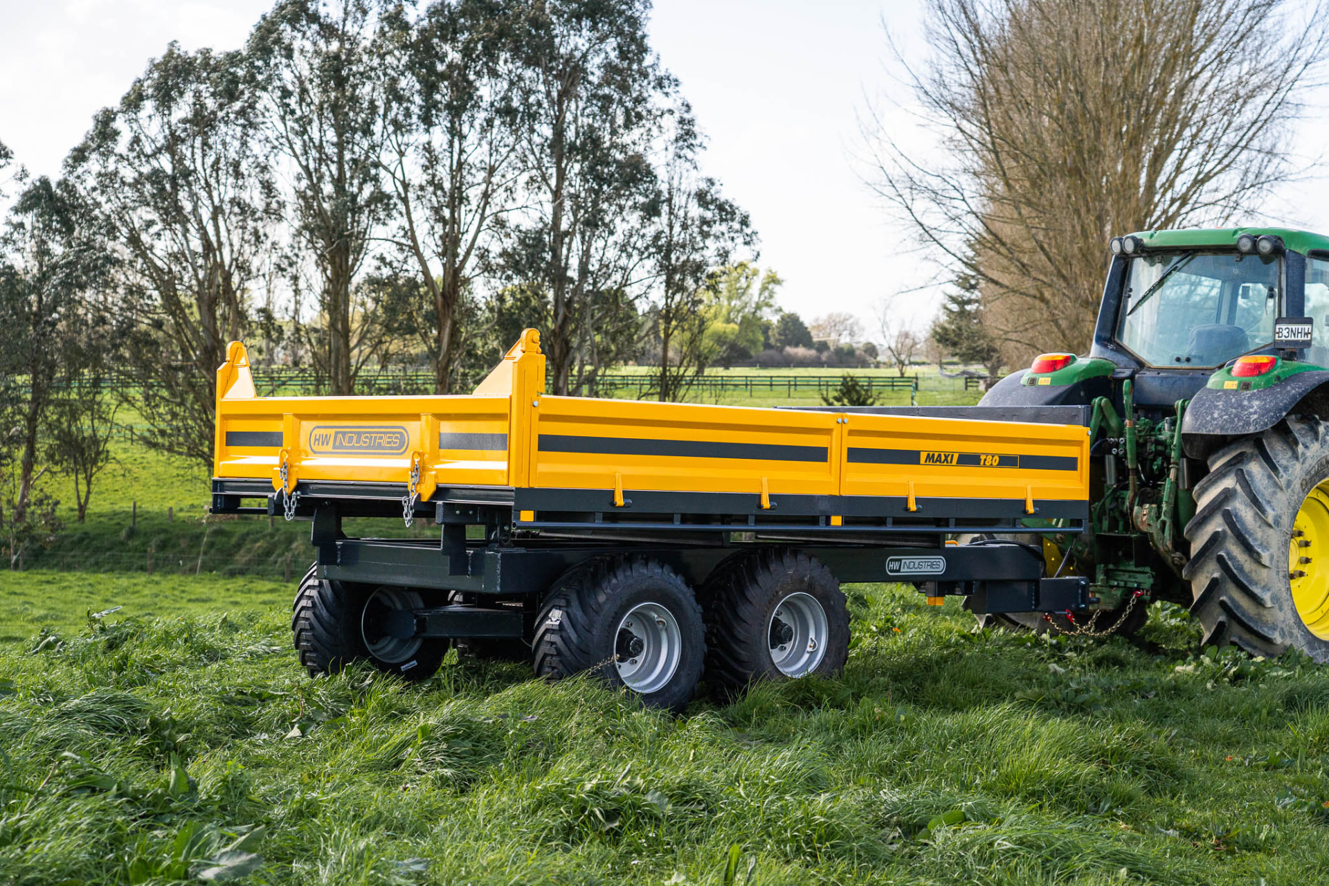 Yellow Maxi T180 tip trailer hitched to a John Deere in long grass