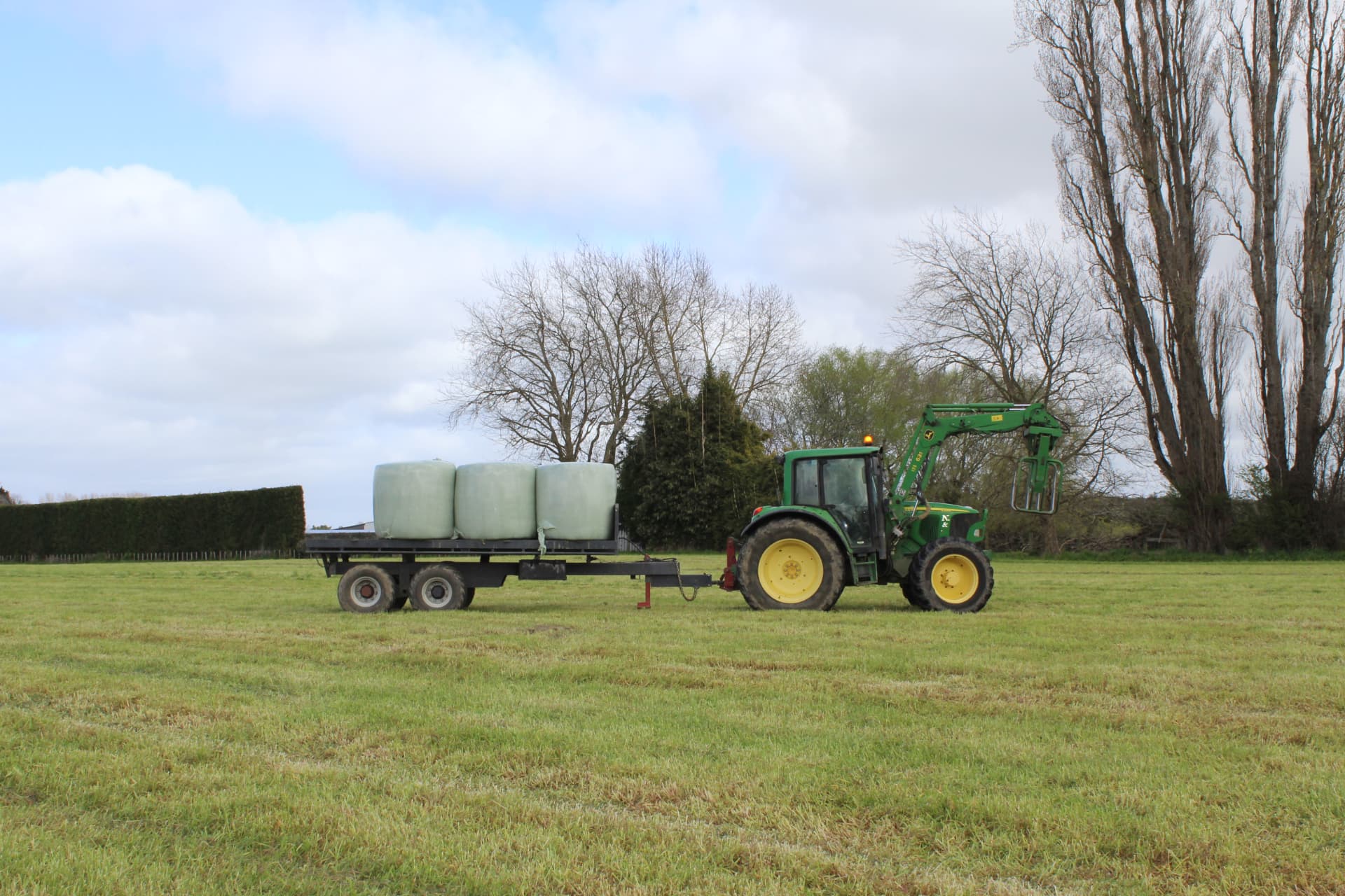 Maxi trailer carrying wrapped bales across a paddock behind a John Deere tractor