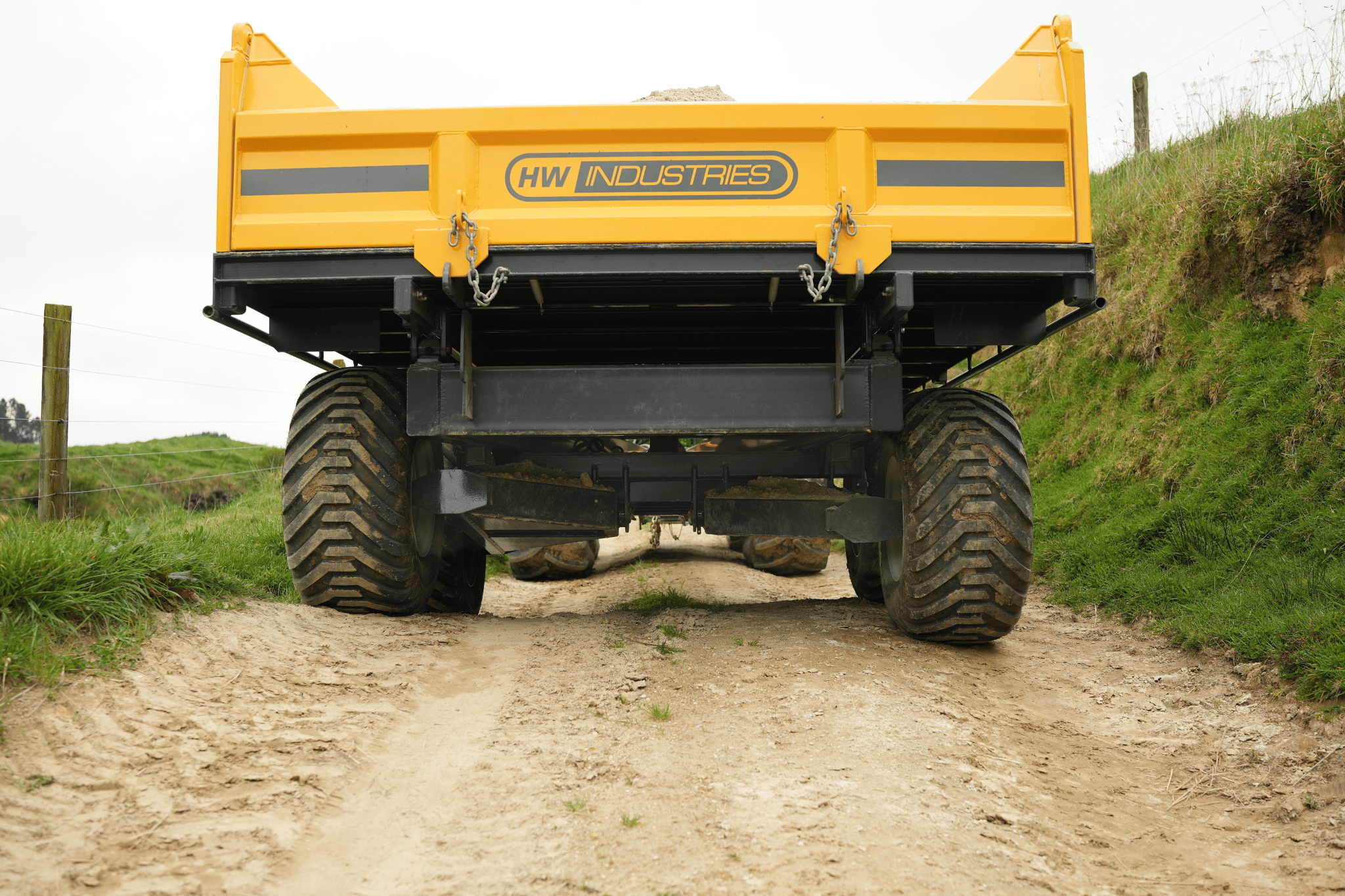Rear view of a yellow Maxi trailer's tandem wheels on a dirt farm track